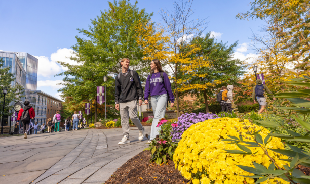 University of Scranton students walking on campus in the fall along a patch of colorful mums