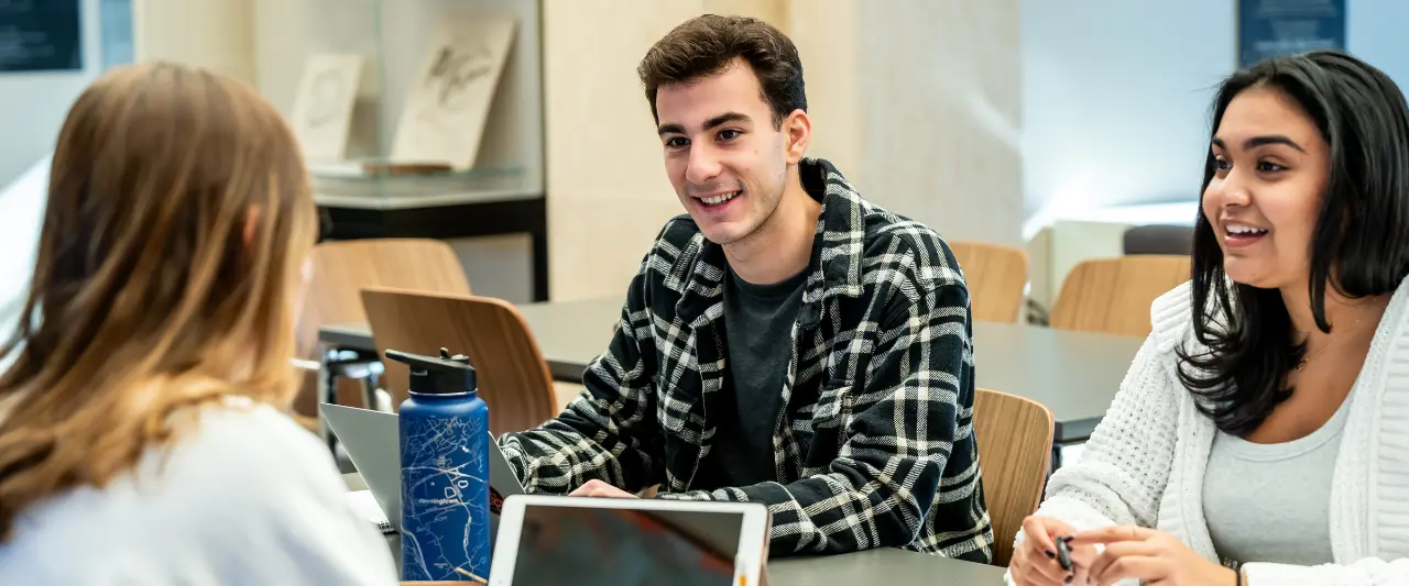 Three Scranton students sit at a table with laptops, smiling and engaging in a group discussion