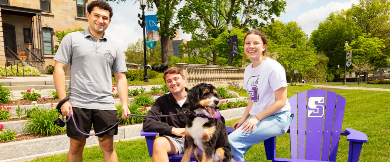 three students smile at the camera with a dog