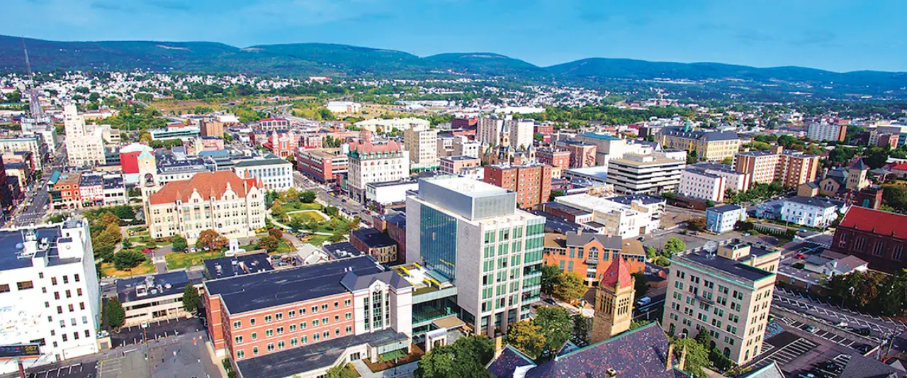 Aerial view of downtown Scranton, Pennsylvania, with modern and historic buildings surrounded by rolling hills under a clear blue sky