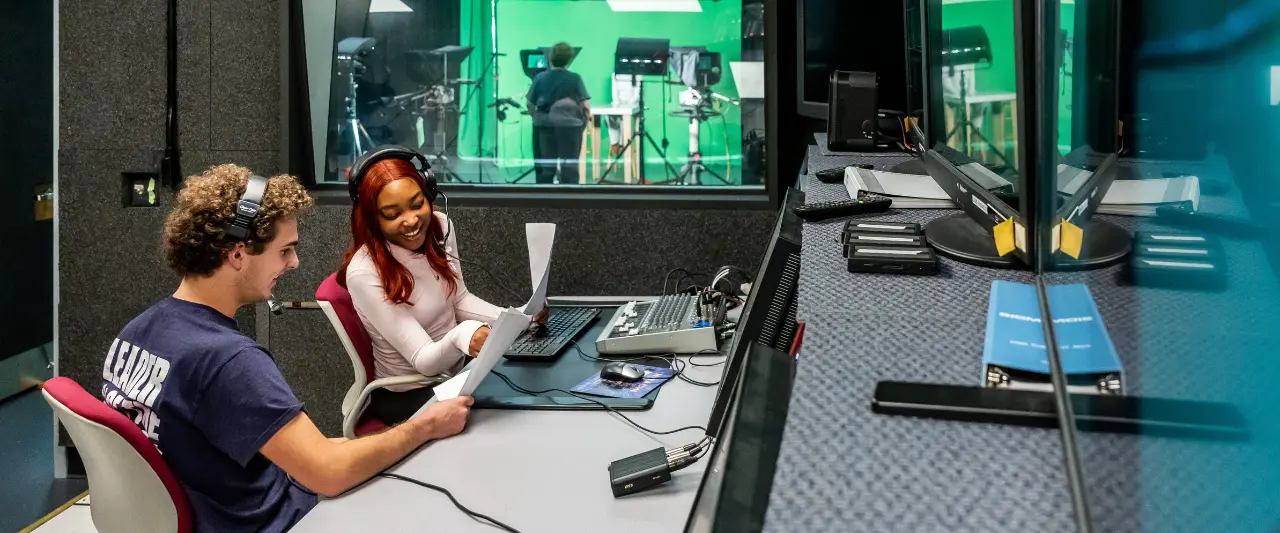 Two Scranton students with headsets review a script at a control desk in a TV studio