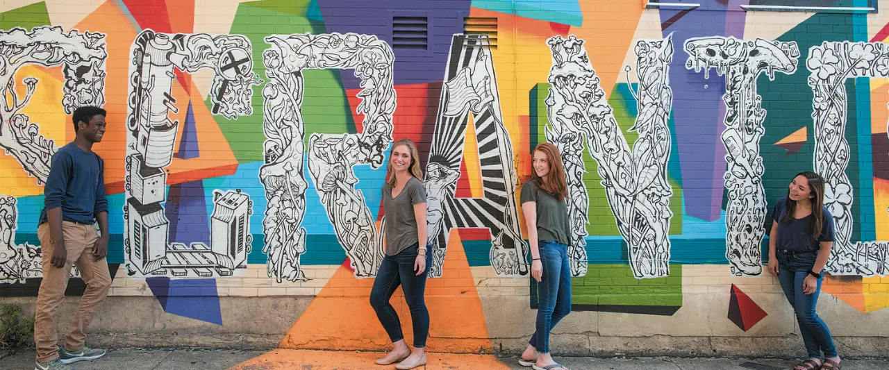 Four Scranton college students posing in front of a large, colorful street mural that spells out SCRANTON