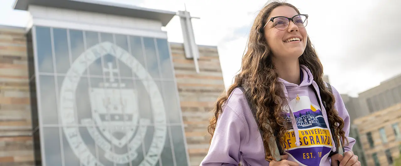 A Scranton female student smiles while looking upward, wearing a purple University of Scranton hoodie